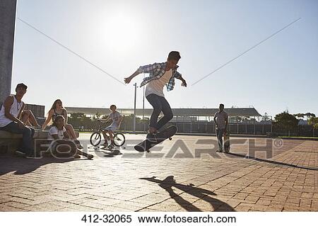 Friends watching teenage boy flipping skateboard at sunny skate park View Large Photo Image Stock Photography - Friends watching teenage boy flipping skateboard at sunny skate park. Fotosearch