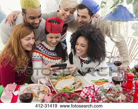 Friends wearing paper crowns taking selfie at Christmas dinner View Large Photo Image Stock Photo - Friends wearing paper crowns taking selfie at Christmas dinner. Fotosearch
