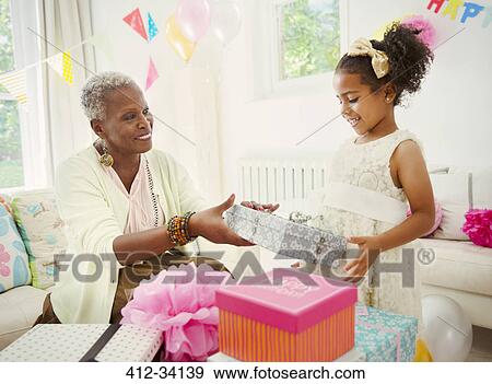Girl giving birthday gift to grandmother at party View Large Photo Image Stock Photo - Girl giving birthday gift to grandmother at party. Fotosearch