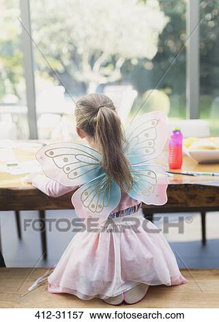 Stock Photo - Girl in fairy wings coloring at dining table. Fotosearch