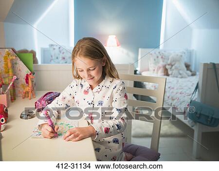 Picture - Girl in pajamas coloring at desk in bedroom. Fotosearch