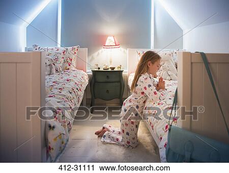 Stock Image - Girl in pajamas saying bedtime prayers at bed. Fotosearch