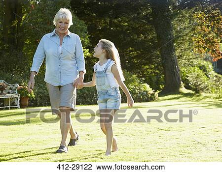 Grandmother and granddaughter holding hands and walking in sunny garden View Large Photo Image Stock Image - Grandmother and granddaughter holding hands and walking in sunny garden. Fotosearch