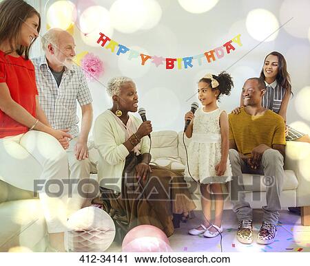 Stock Image - Grandmother and granddaughter singing karaoke with microphones at birthday party. Fotosearch