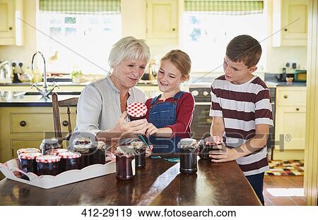 Stock Photo - Grandmother canning jam with grandchildren in kitchen. Fotosearch