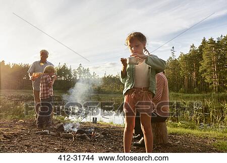 Picture - Grandparents and grandchildren cooking at lakeside in woods. Fotosearch