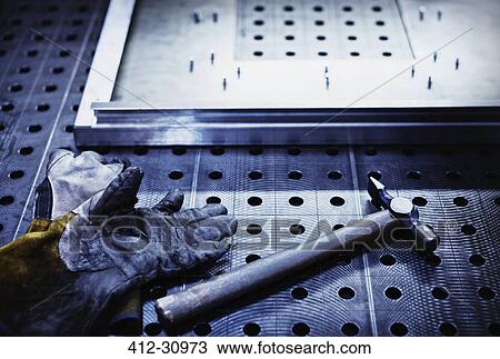 Stock Image - Hammer and gloves on steel in steel factory. Fotosearch
