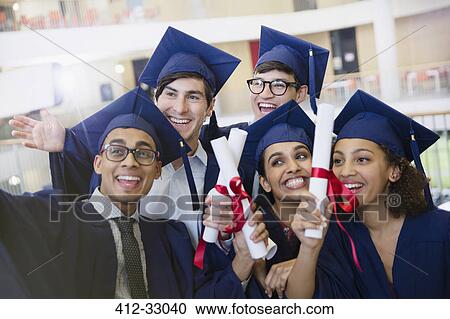 Happy college students in cap and gown holding diplomas posing for selfie View Large Photo Image Stock Image - Happy college students in cap and gown holding diplomas posing for selfie. Fotosearch