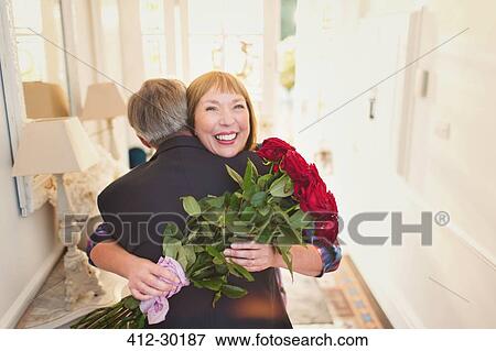 Happy women receiving rose bouquet and hugging husband View Large Photo Image Stock Photo - Happy women receiving rose bouquet and hugging husband. Fotosearch