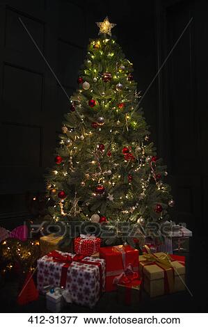 Stock Photo - Illuminated Christmas tree surrounded by gifts in dark room. Fotosearch