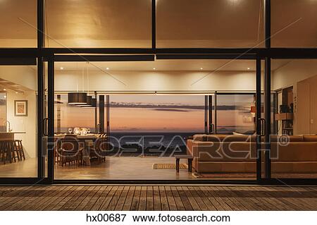 Illuminated home showcase interior overlooking ocean at sunset View Large Photo Image Stock Photo - Illuminated home showcase interior overlooking ocean at sunset. Fotosearch