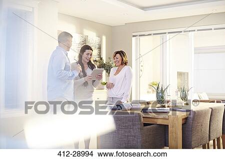 Picture - Interior designer using digital tablet in consultation with couple in dining room. Fotosearch