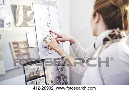 Stock Image - Interior designers discussing blueprints hanging in office. Fotosearch