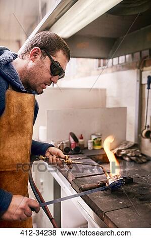 Stock Photo - Jeweler heating metal using torch in workshop. Fotosearch