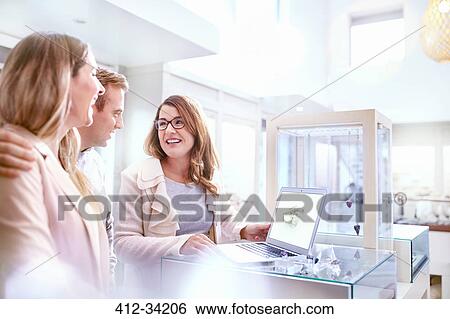 Jeweler with laptop showing wedding rings to couple in jewelry store View Large Photo Image Stock Photograph - Jeweler with laptop showing wedding rings to couple in jewelry store. Fotosearch