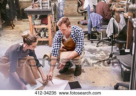 Stock Photography - Jewelers brainstorming with digital tablet and blueprint in workshop. Fotosearch