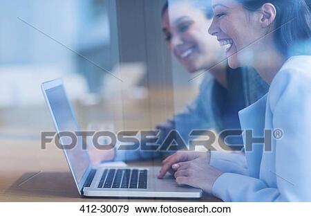 Stock Photo - Laughing businesswomen working at laptop. Fotosearch