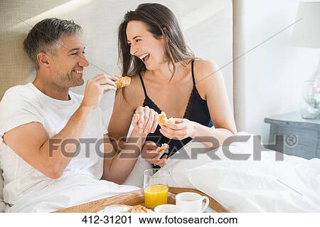 Laughing couple enjoying breakfast in bed View Large Photo Image Stock Image - Laughing couple enjoying breakfast in bed. Fotosearch