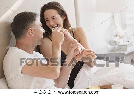 Stock Photo - Laughing couple enjoying breakfast in bed. Fotosearch