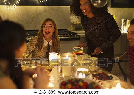 Laughing friends enjoying cake at candlelight Christmas dinner party View Large Photo Image Stock Photo - Laughing friends enjoying cake at candlelight Christmas dinner party. Fotosearch