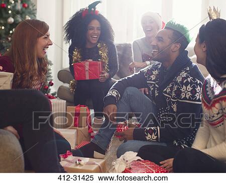 Stock Photography - Laughing friends opening Christmas gifts in living room. Fotosearch