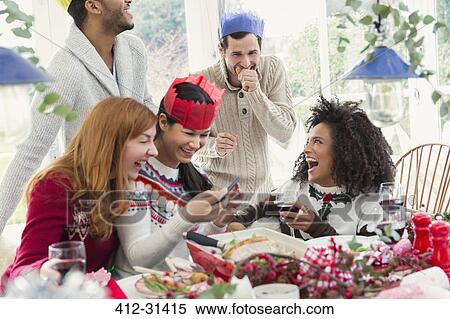 Laughing friends wearing paper crowns at Christmas dinner View Large Photo Image Stock Photography - Laughing friends wearing paper crowns at Christmas dinner. Fotosearch