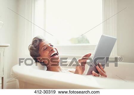 Laughing mature woman using digital tablet in bathtub View Large Photo Image Stock Photo - Laughing mature woman using digital tablet in bathtub. Fotosearch