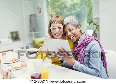 Laughing mature women sharing digital tablet at breakfast table View Large Photo Image Stock Image - Laughing mature women sharing digital tablet at breakfast table. Fotosearch