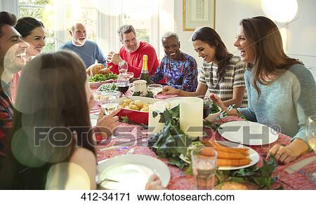 Stock Image - Laughing multi-ethnic family enjoying Christmas dinner at table. Fotosearch