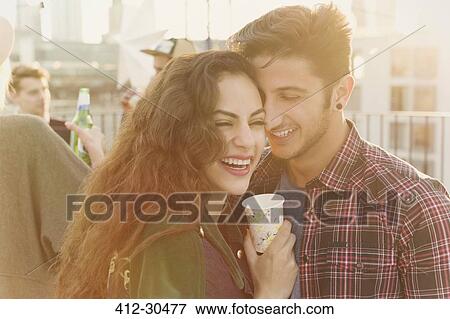 Laughing young couple hugging at rooftop party View Large Photo Image Stock Photo - Laughing young couple hugging at rooftop party. Fotosearch