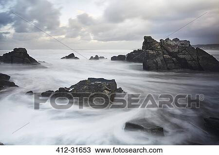 Stock Image - Long exposure ocean swirling around rocks, Devon, United Kingdom. Fotosearch