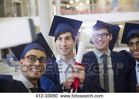 Stock Image - Male college graduates in cap and gown with diploma taking selfie. Fotosearch