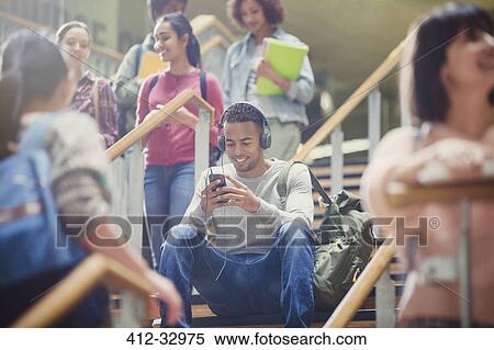 Male college student listening to mp3 player in busy stairway View Large Photo Image Stock Photography - Male college student listening to mp3 player in busy stairway. Fotosearch