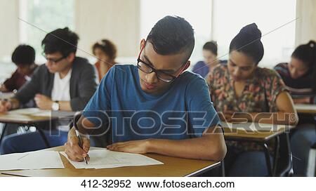Stock Image - Male college student taking test at desk in classroom. Fotosearch