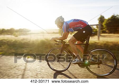Stock Image - Male cyclist cycling on sunny sunrise rural road. Fotosearch