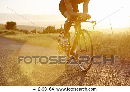 Male cyclist riding bike on sunny sunrise rural road View Large Photo Image Picture - Male cyclist riding bike on sunny sunrise rural road. Fotosearch
