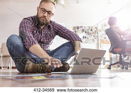 Male design professional reviewing proofs at laptop on office floor View Large Photo Image Stock Photo - Male design professional reviewing proofs at laptop on office floor. Fotosearch