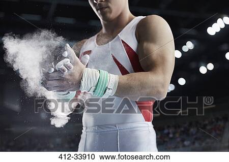 Stock Image - Male gymnast applying chalk powder to hands. Fotosearch