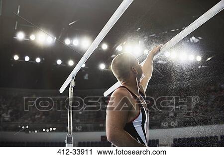 Stock Image - Male gymnast applying chalk powder to parallel bars. Fotosearch