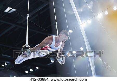 Picture - Male gymnast performing on gymnastics rings in arena. Fotosearch