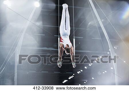 Stock Photo - Male gymnast performing upside-down on gymnastics rings in arena. Fotosearch