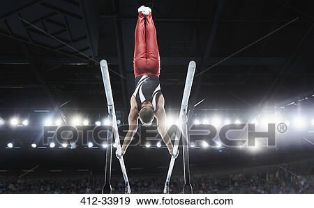Stock Photo - Male gymnast performing upside-down handstand on parallel bars in arena. Fotosearch