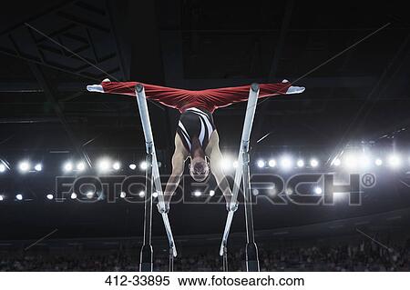 Stock Photography - Male gymnast performing upside-down splits on parallel bars in arena. Fotosearch