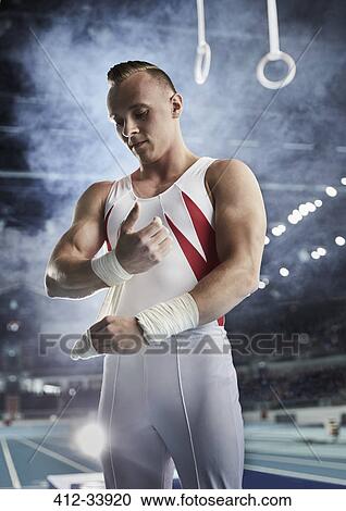 Male gymnast wrapping wrists below gymnastics rings in arena View Large Photo Image Stock Image - Male gymnast wrapping wrists below gymnastics rings in arena. Fotosearch