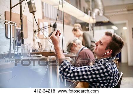 Male jeweler listening to music with headphones working in workshop View Large Photo Image Stock Photo - Male jeweler listening to music with headphones working in workshop. Fotosearch