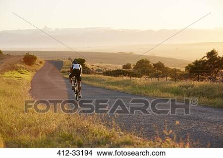 Male triathlete cyclist cycling on sunny rural road at sunrise View Large Photo Image Picture - Male triathlete cyclist cycling on sunny rural road at sunrise. Fotosearch