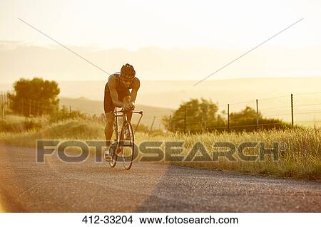 Picture - Male triathlete cyclist cycling on sunny rural road at sunrise. Fotosearch