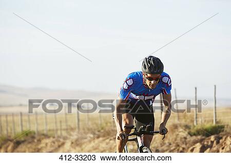 Stock Image - Male triathlete cyclist cycling on sunny rural road at sunrise. Fotosearch
