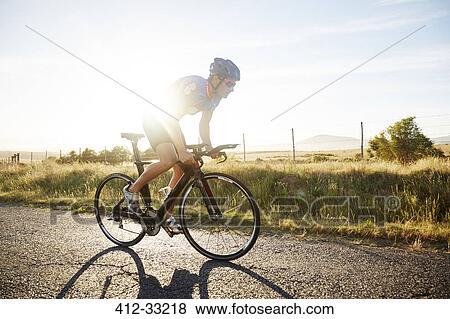 Male triathlete cyclist cycling on sunny rural road at sunrise View Large Photo Image Stock Photo - Male triathlete cyclist cycling on sunny rural road at sunrise. Fotosearch