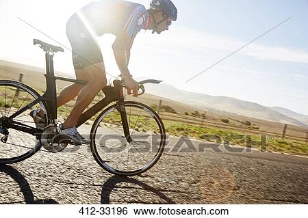 Stock Photograph - Male triathlete cyclist cycling on sunny rural road at sunrise. Fotosearch